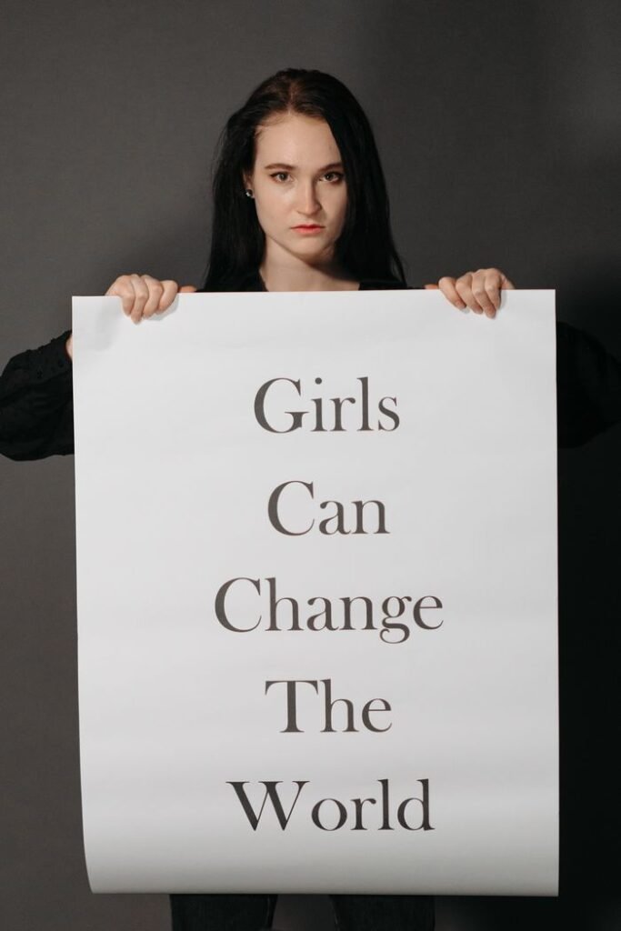 A woman holds a powerful sign stating 'Girls Can Change the World' on a gray background.